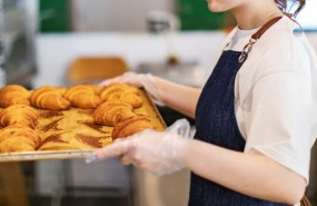 nainen laittaa croisantteja täynnä olevaa uunipeltiä kärryyn