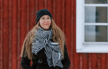 Nainen seisoo ulkona punaisen puutalon edessä