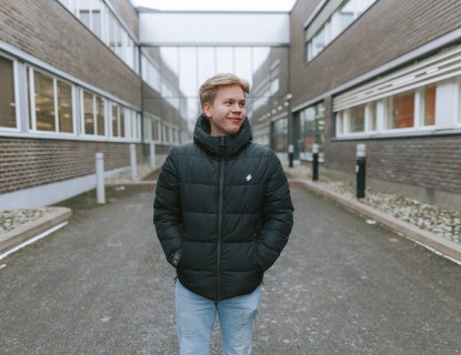 Jimi Leino seisomassa HAMKin kampuksella Riihimäellä ulkona kahden tiilirakennuksen seinien välissä kulkevalla hiekkakäytävällä